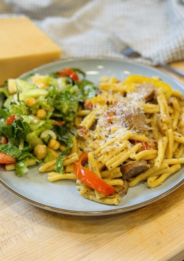 final dish of sausage and pepper pasta on a plate with salad pairing