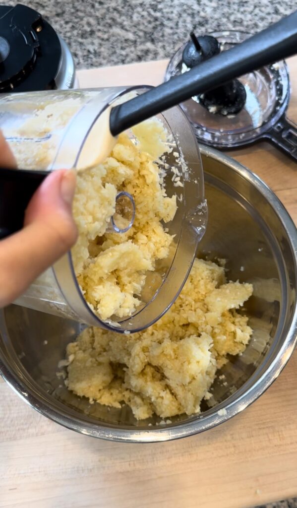 scraping the garlic from the food processor to a bowl