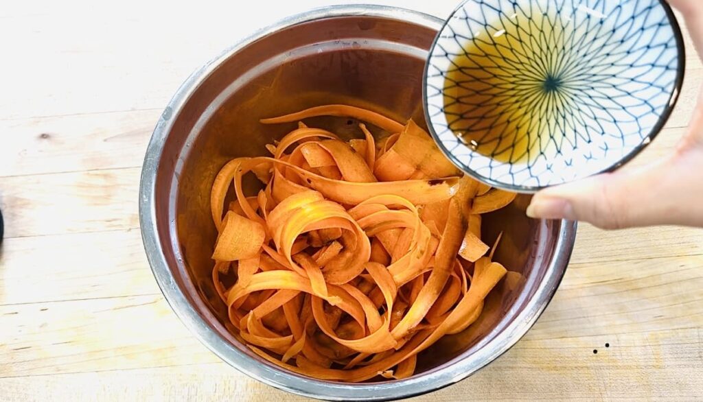 adding soy sauce and sesame oil to carrot salad served carrot ribbons