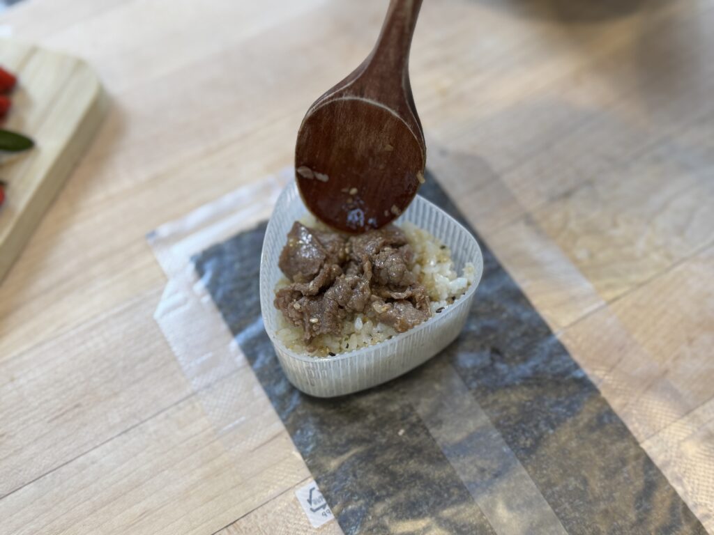 Japanese onigiri with beef bulgogi being added over a layer of rice