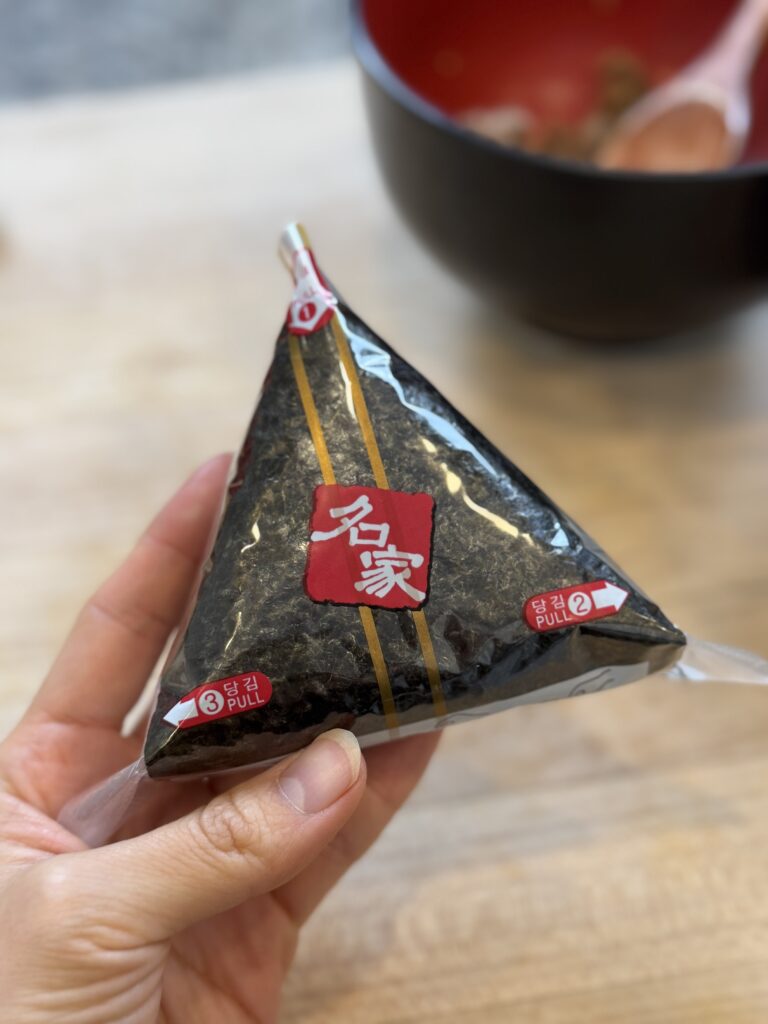 Triangle shaped onigiri wrapped in seaweed and store-bought onigiri wrapper held by hand.