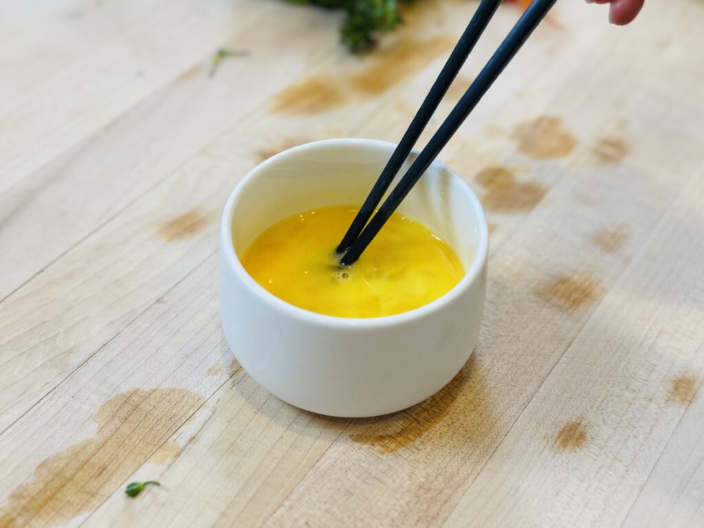 Chopsticks stirring raw egg in a small white bowl