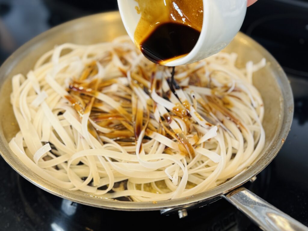 Pouring mixed soy sauce on rice stick noodles on metal pan