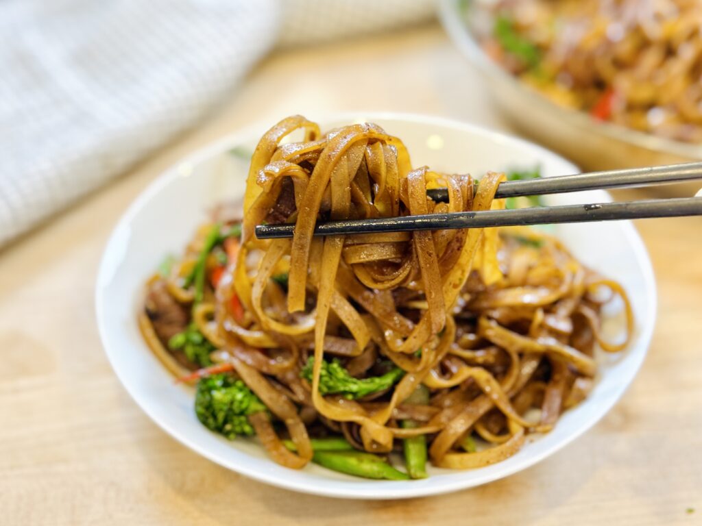 Thai stir-fried noodles lifted with chopsticks over a plate.