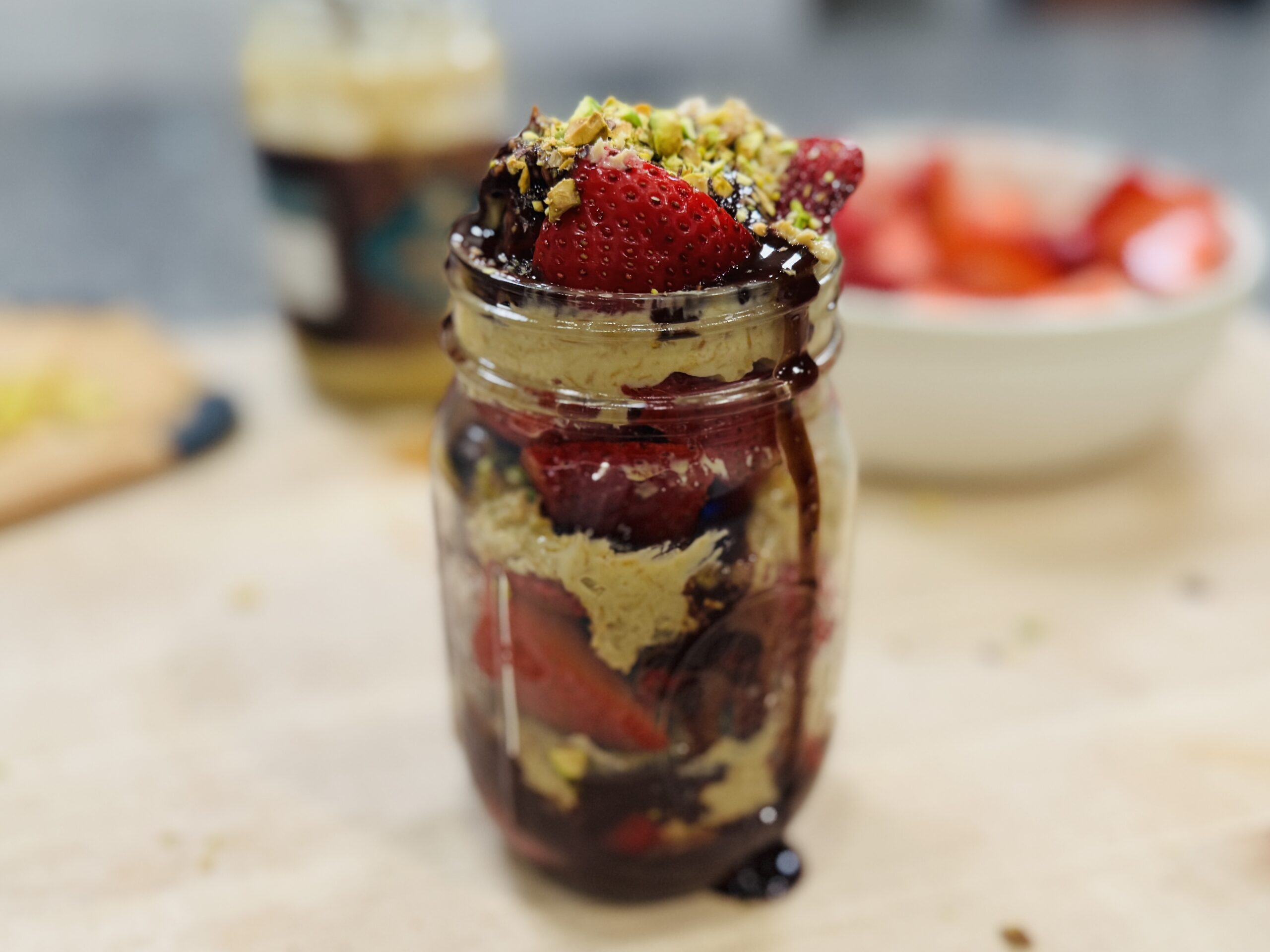 Jar of layered fresh strawberries, crunchy pistachio cream, melted chocolate, and crushed pistachios
