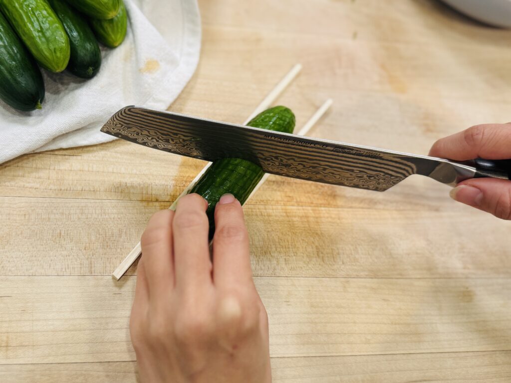 Baby cucumber being spiral-cut between two chopsticks — step by step diagonal and straight cuts