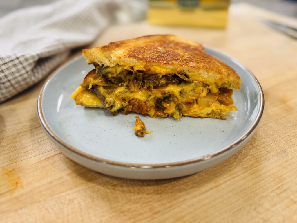 Kimchi grilled cheese with bulgogi sliced diagonally on a cutting board — golden sourdough with melted American cheese, caramelized kimchi, and bulgogi filling visible in the cross section