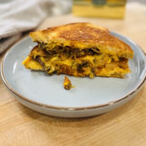 Kimchi grilled cheese with bulgogi sliced diagonally on a cutting board — golden sourdough with melted American cheese, caramelized kimchi, and bulgogi filling visible in the cross section