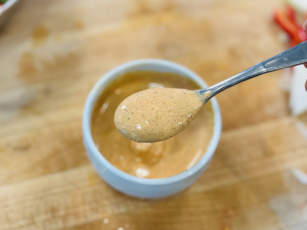 Homemade creamy sauce for Mexican hot dogs in a bowl with a spoonful lifted to show the smooth, creamy texture — made with sour cream, mayo, ketchup, mustard, and spices