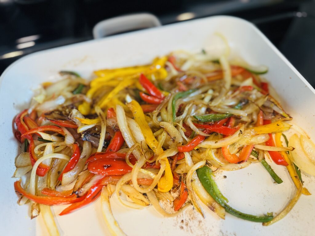 Sliced bell peppers, onions, and jalapeño caramelizing in a pan over medium heat, golden and softened after 6 to 10 minutes