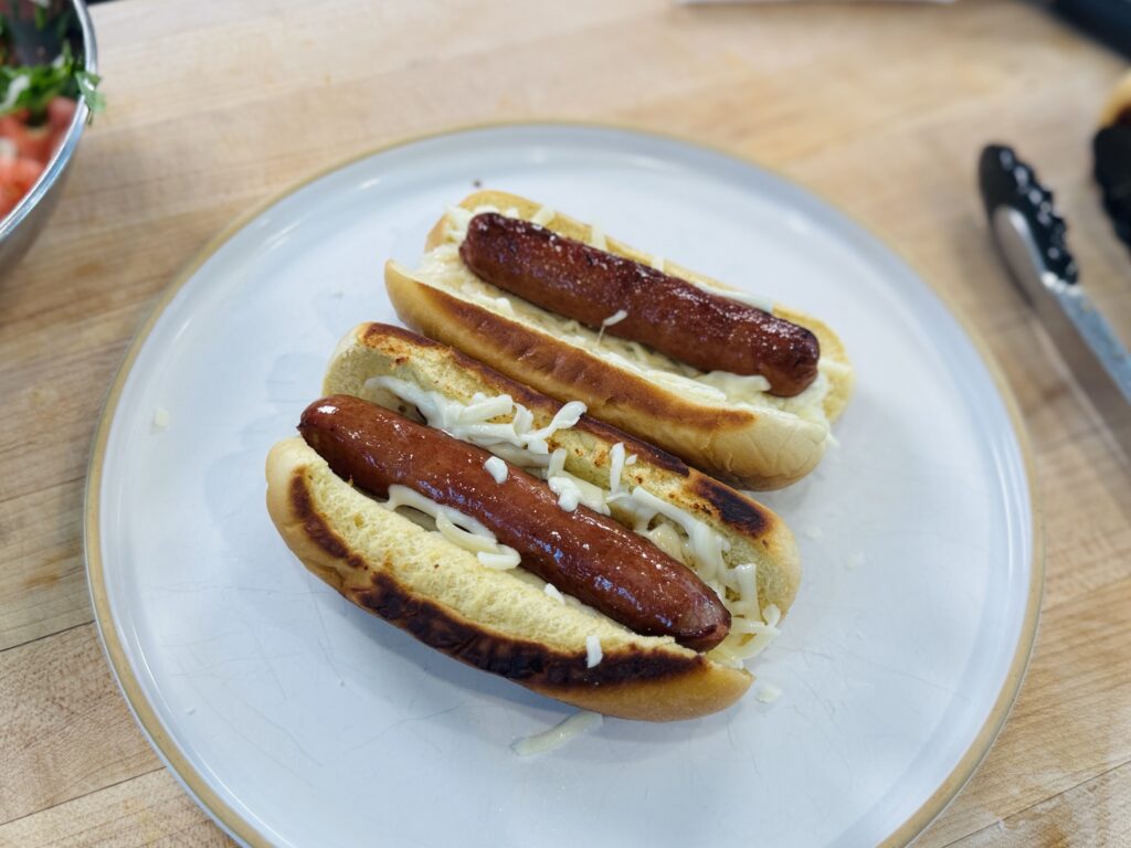 Mexican hot dog assembly — shredded mozzarella cheese melting inside a toasted bun with a cooked hot dog placed directly on top
