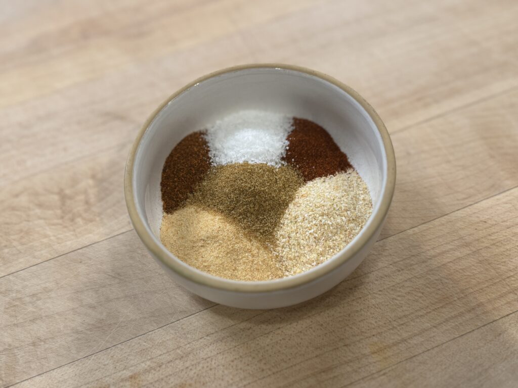 Garlic powder, onion powder, paprika, cumin, chili powder, and salt measured into a small bowl before mixing into the seasoning blend