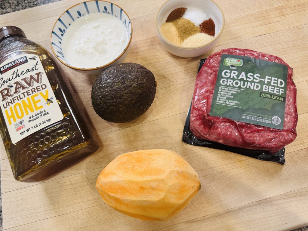 Ingredients for ground beef sweet potato cottage cheese bowl — sweet potato, ground beef, cottage cheese, avocado, olive oil, hot honey, kimchi, and red pepper flakes arranged on a surface