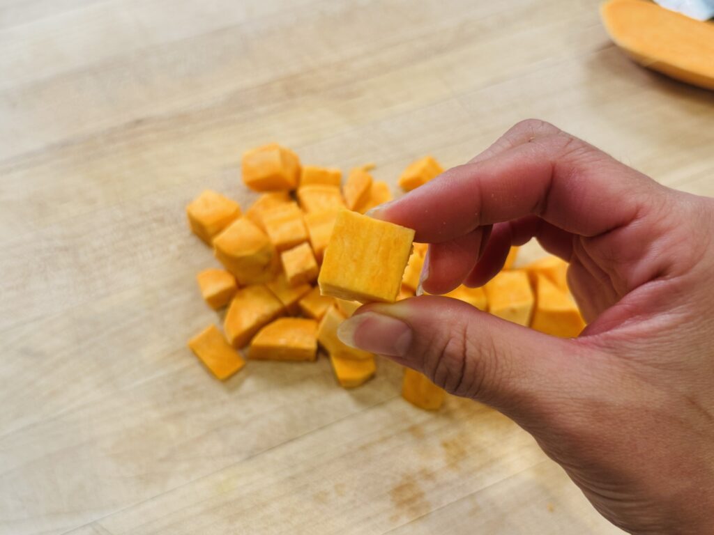 Raw sweet potato chopped into half-inch cubes on a cutting board, showing the correct size for even roasting