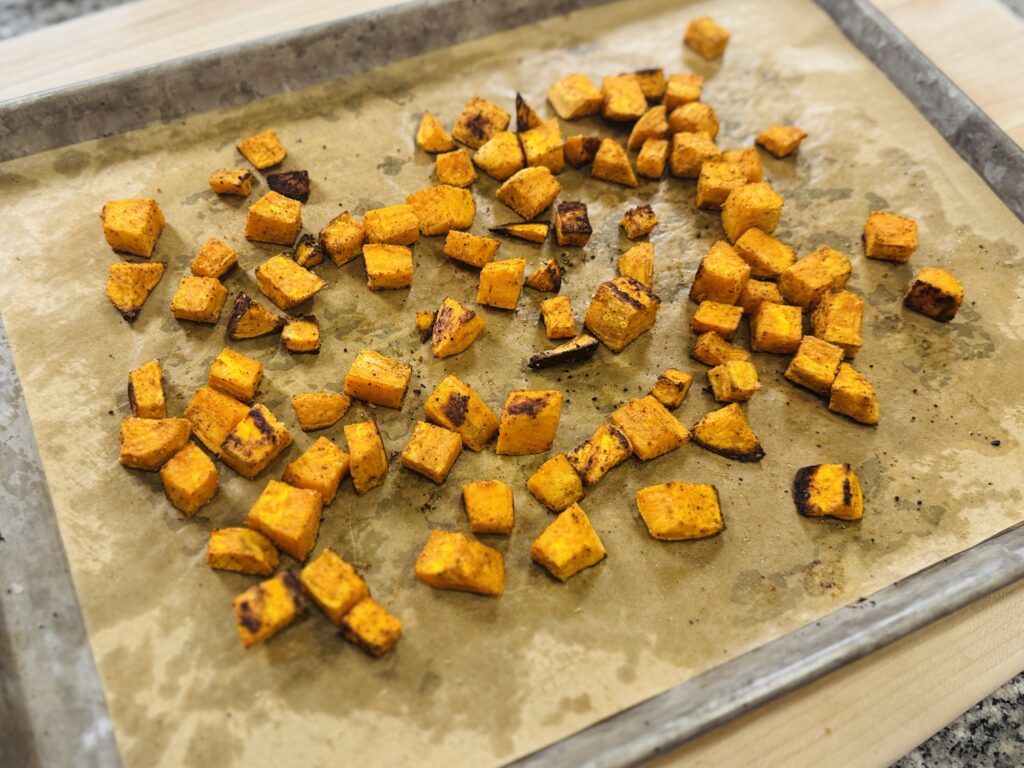 Roasted sweet potato cubes on a parchment-lined baking pan, caramelized and slightly charred at the edges after 30 minutes at 400°F