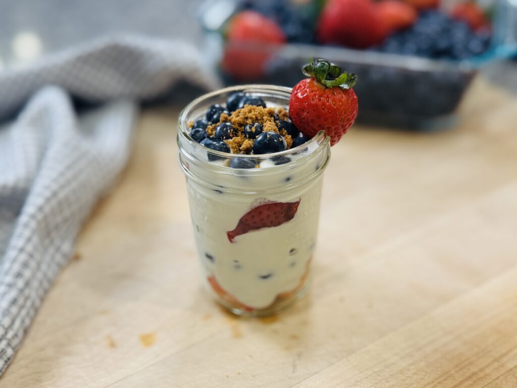 High protein berry trifle in a small mason jar — layers of whipped cottage cheese and fresh berries, topped with crushed Biscoff cookies and a fresh strawberry on the rim