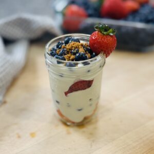 High protein berry trifle in a small mason jar — layers of whipped cottage cheese and fresh berries, topped with crushed Biscoff cookies and a fresh strawberry on the rim
