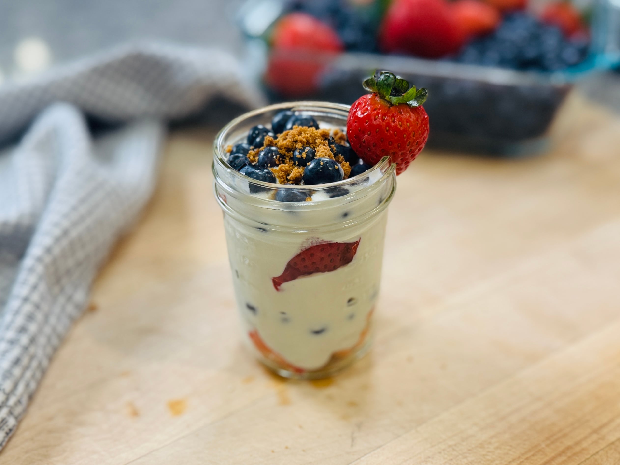 High protein berry trifle in a small mason jar — layers of whipped cottage cheese and fresh berries, topped with crushed Biscoff cookies and a fresh strawberry on the rim