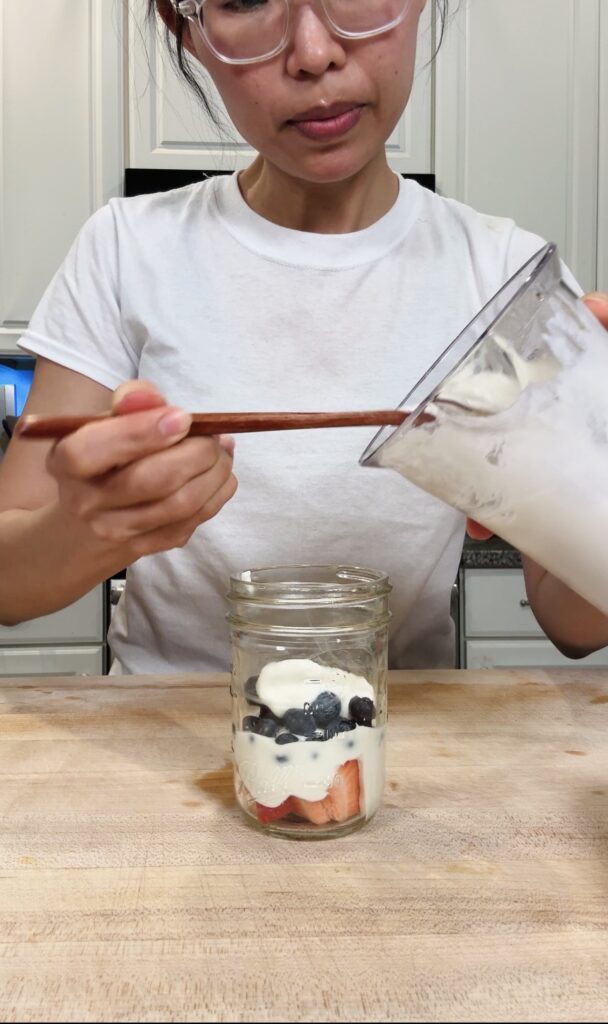 Olivia layering whipped cottage cheese and fresh berries into a small mason jar to assemble the high protein berry trifle