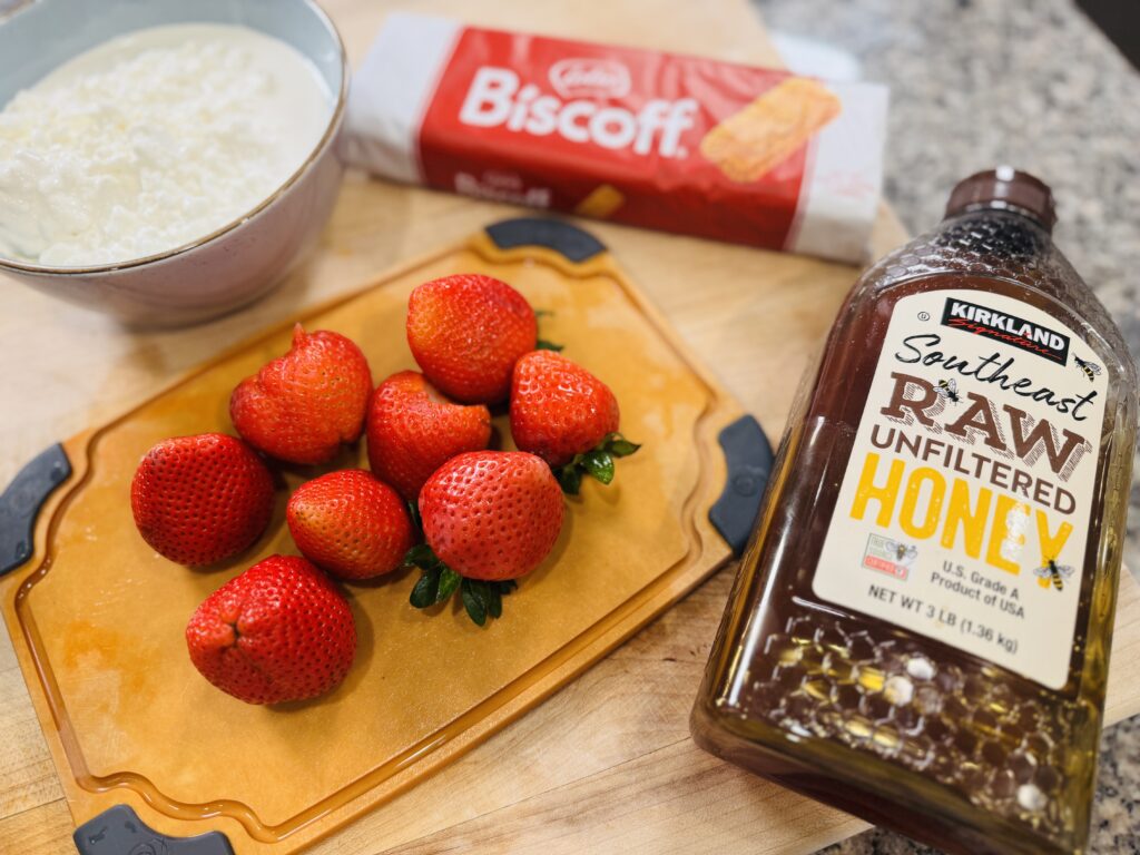 Ingredients for strawberry Biscoff cottage cheese ice cream — cottage cheese, fresh strawberries, honey, and Biscoff cookies arranged on a surface