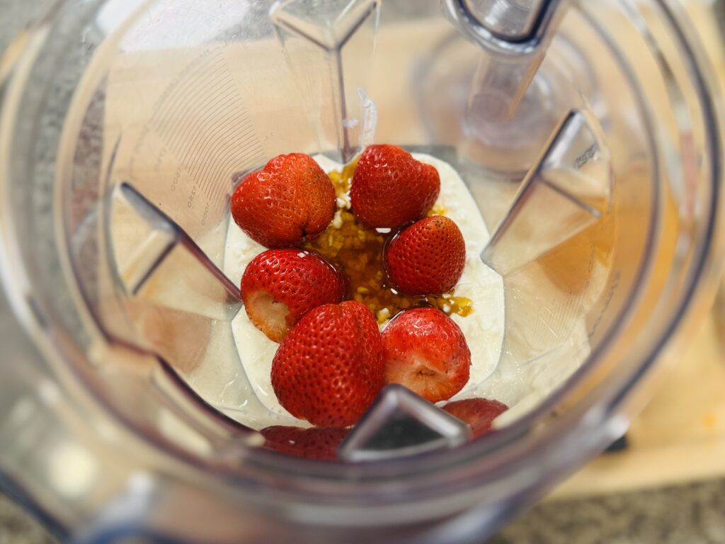 Overhead shot of a blender filled with cottage cheese, fresh strawberries, and honey — ready to be blended into the ice cream base