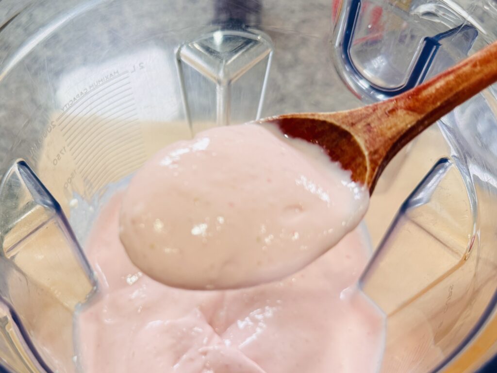 Close-up of a spoonful of blended strawberry cottage cheese mixture showing a smooth, creamy texture before freezing