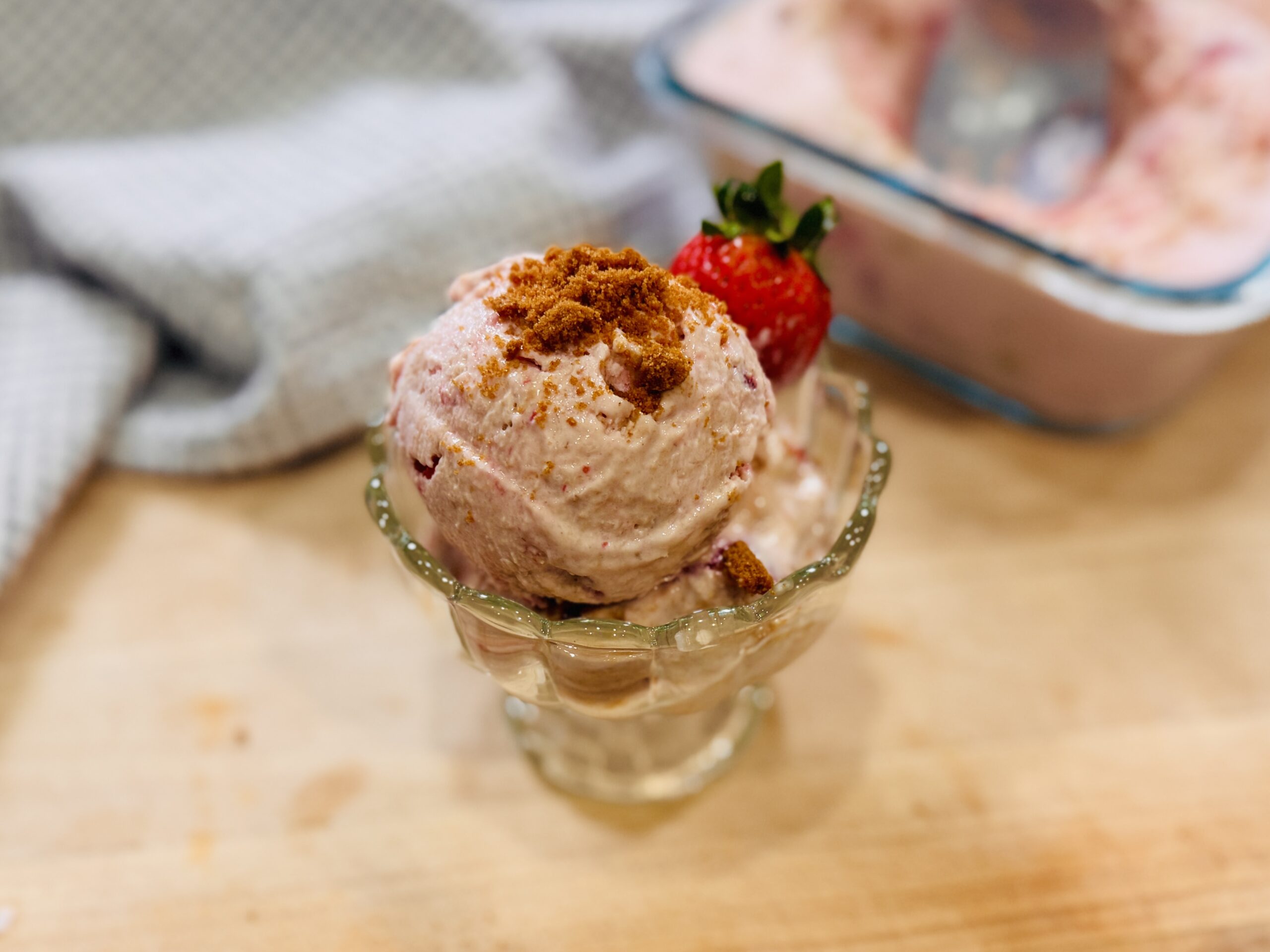 Strawberry Biscoff cottage cheese ice cream scooped into a bowl, garnished with crushed Biscoff cookies and a fresh strawberry on the rim