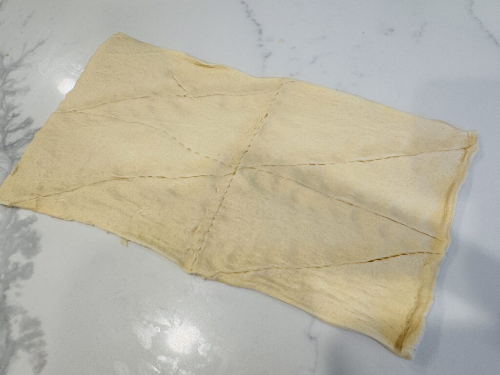 Crescent dough rolled out flat on a surface with the perforated seams gently pinched together to create one unified piece of dough