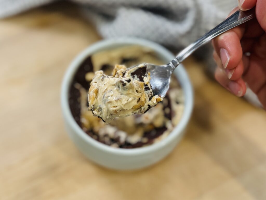 Spoonful of magic shell yogurt with cracked chocolate shell and bowl in background
