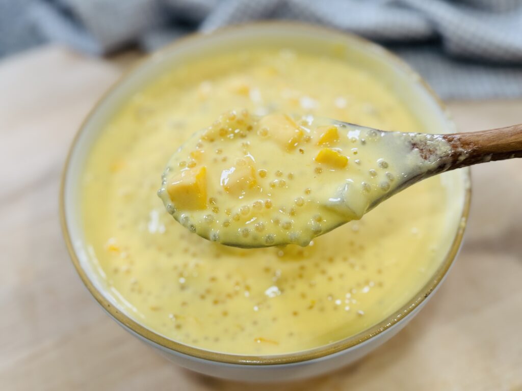 Close-up of a spoonful of mango sago lifted over the bowl showing mango, sago pearls, and coconut jelly