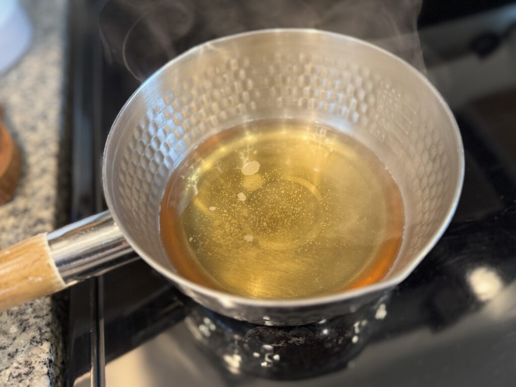 Apple juice heating in a small pot on the stovetop until steaming but not boiling
