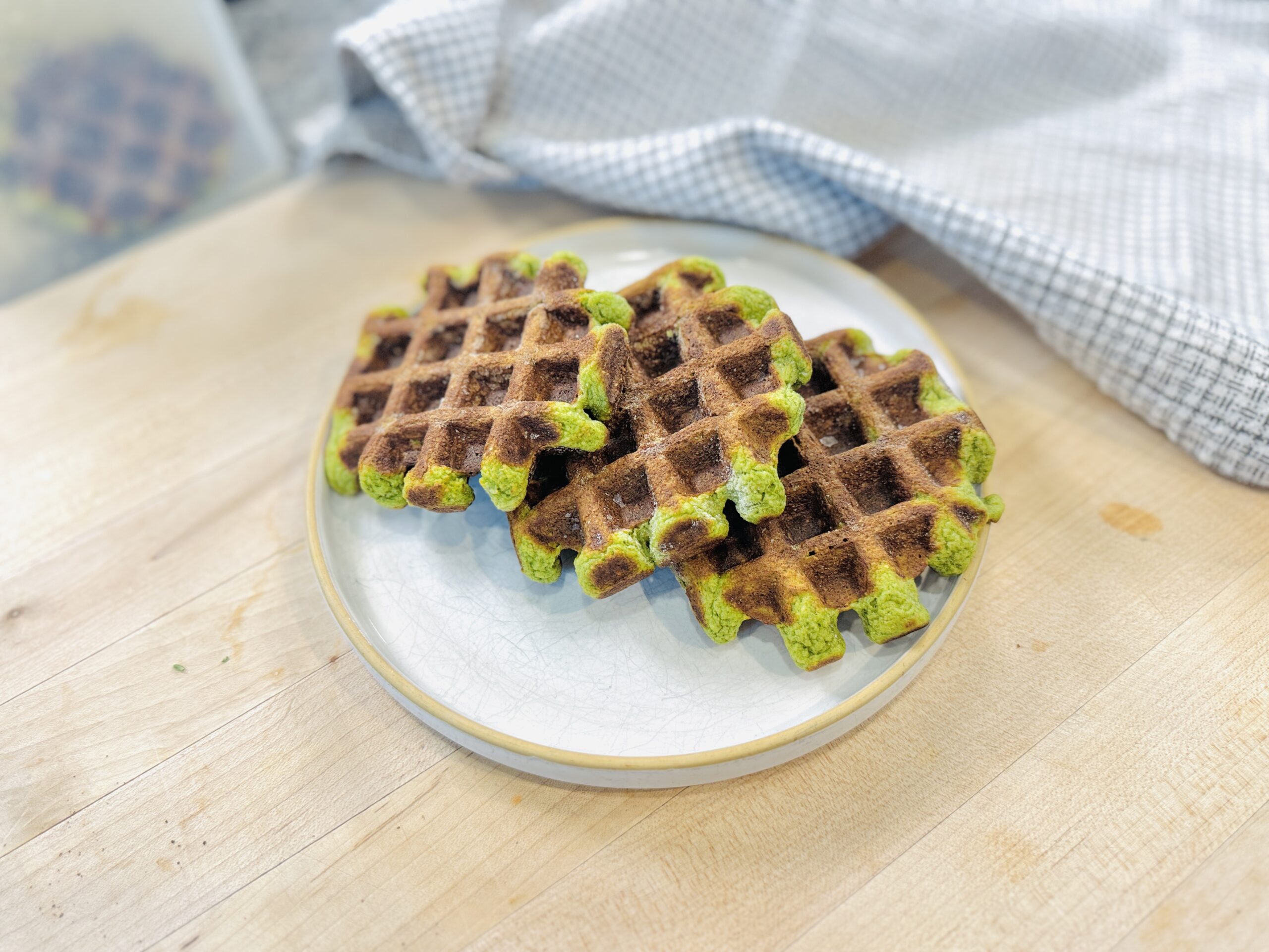 Three spinach banana oat waffles stacked on a plate, showing the green flecks from spinach throughout