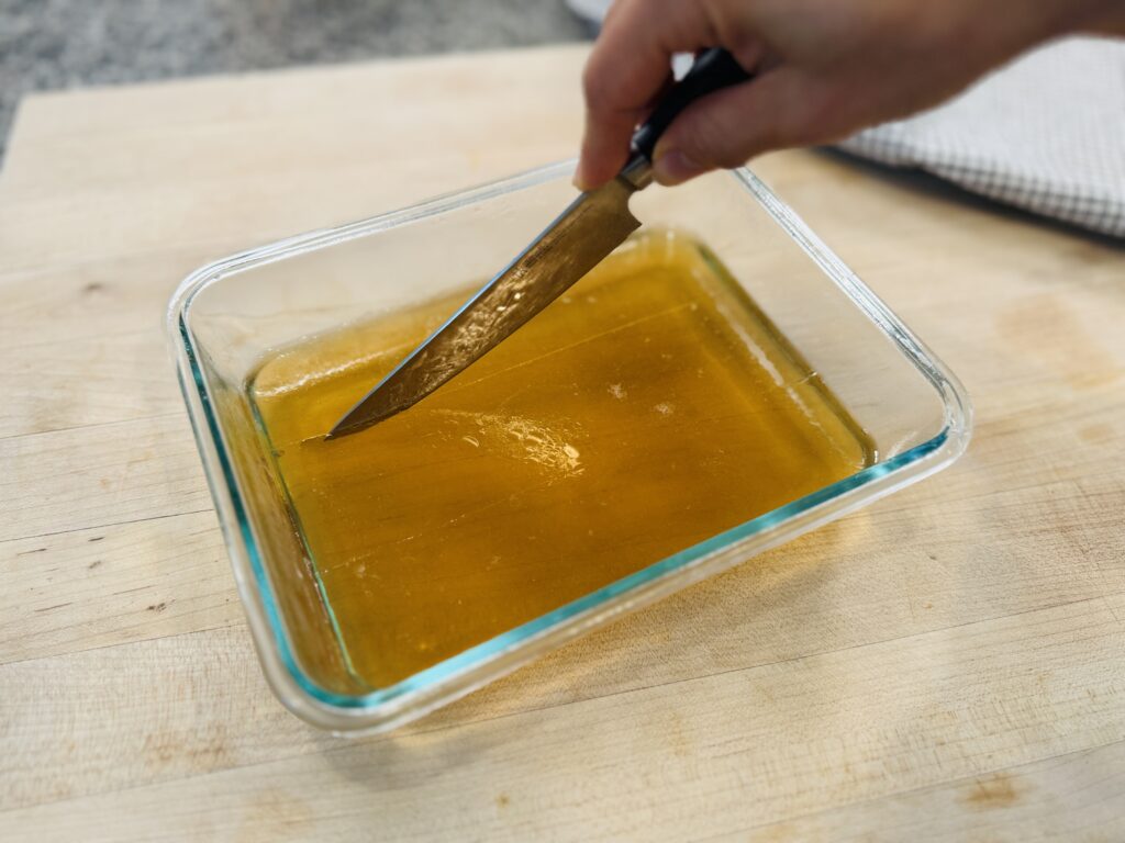 Knife slicing set apple gelatin gummy mixture into individual squares inside a glass container