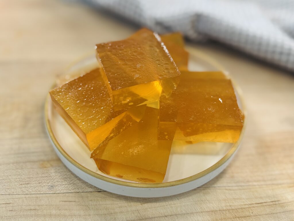 Close-up of a homemade apple protein gummy square with more gummy squares on a plate in the background
