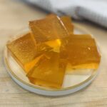 Close-up of a homemade apple protein gummy square with more gummy squares on a plate in the background