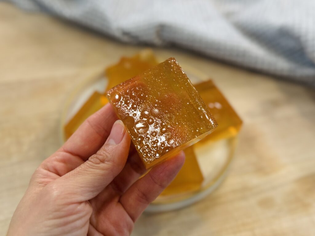 Close-up of a homemade apple protein gummy square with more gummy squares on a plate in the background