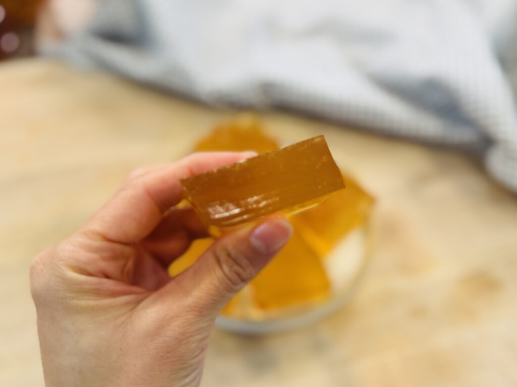 Side view close-up of a homemade apple protein gummy square showing its thickness and jiggly texture