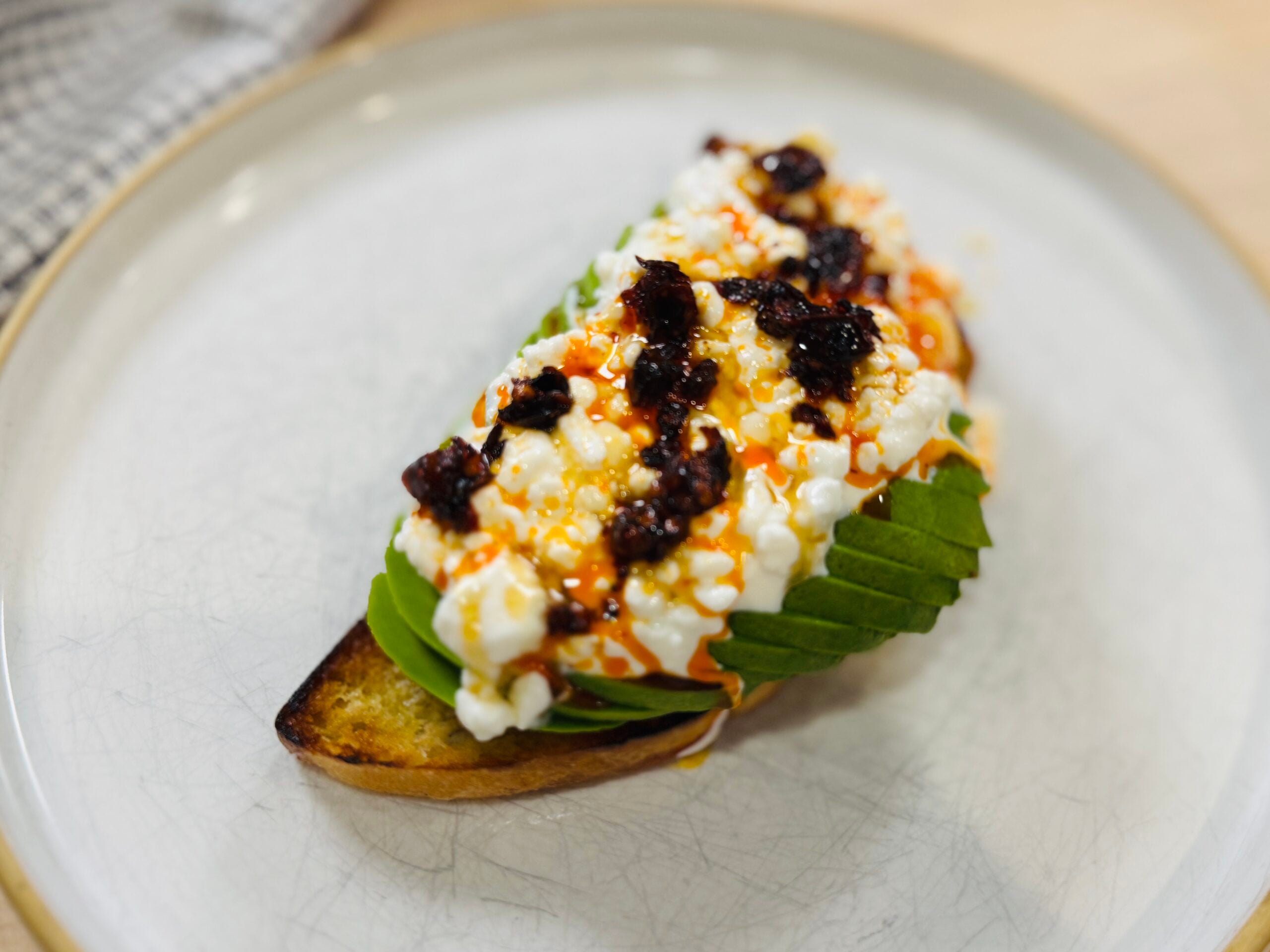 Cottage cheese toast with sliced avocado, chili oil, and honey on toasted sourdough